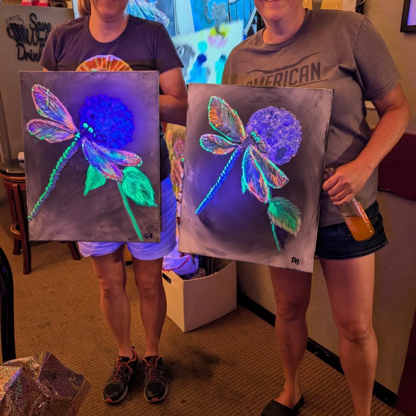 Two guests holding glowing dragonfly paintings