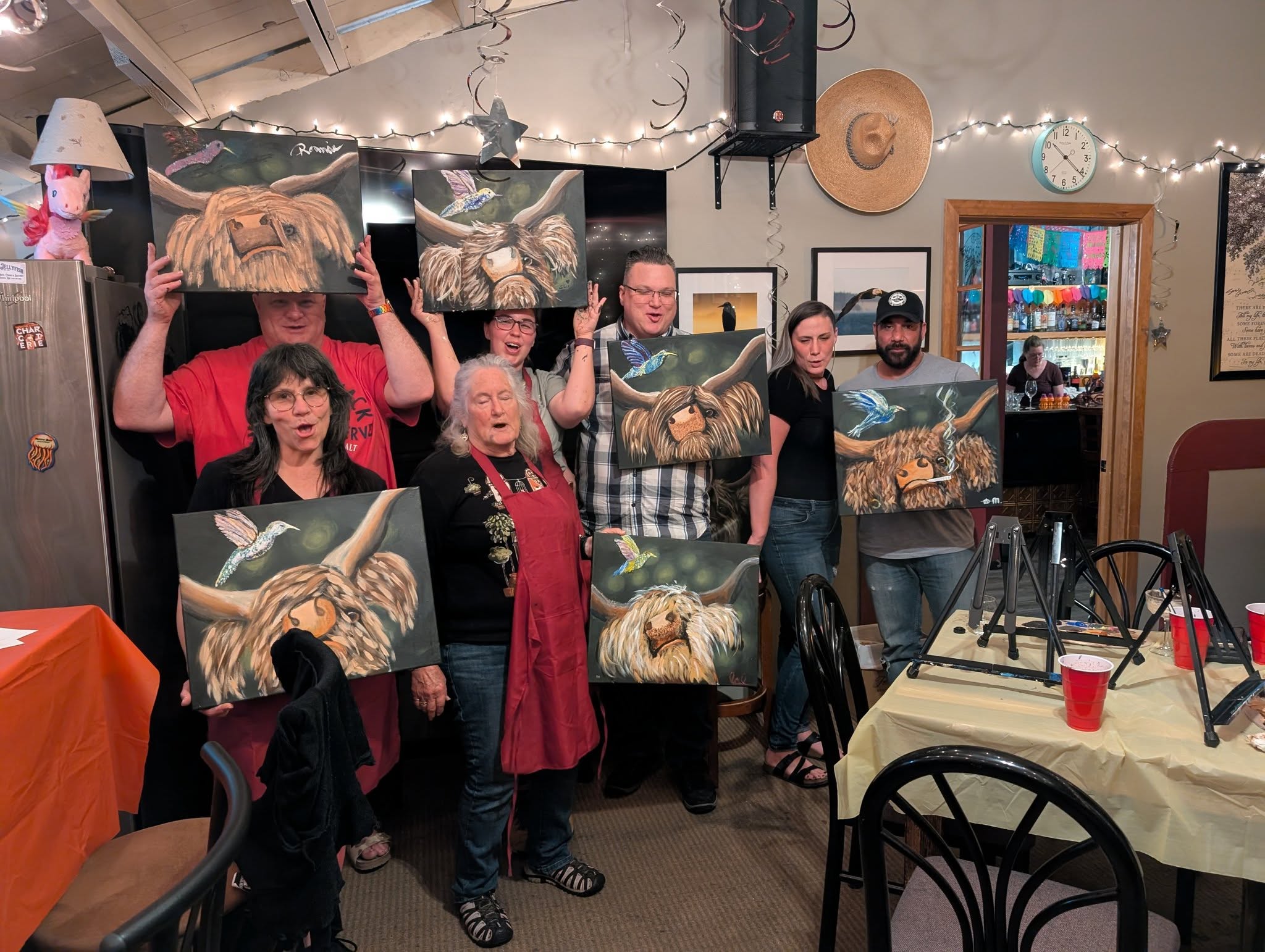 Paint night guests posing with paintings in a restaurant