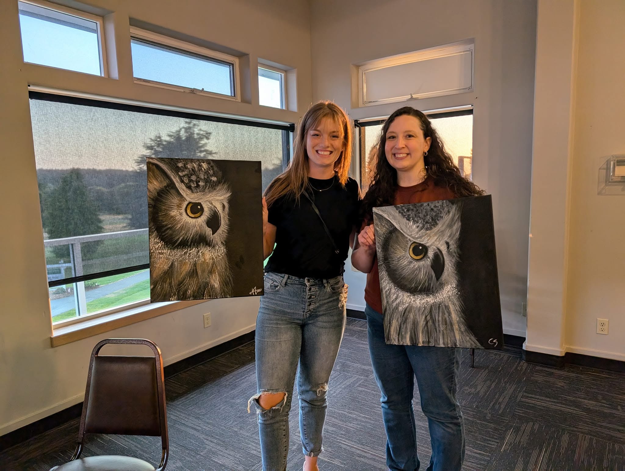 Two guests holding owl paintings by the window