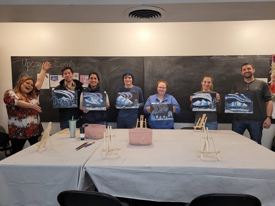 Group holding finished paintings in front of a window