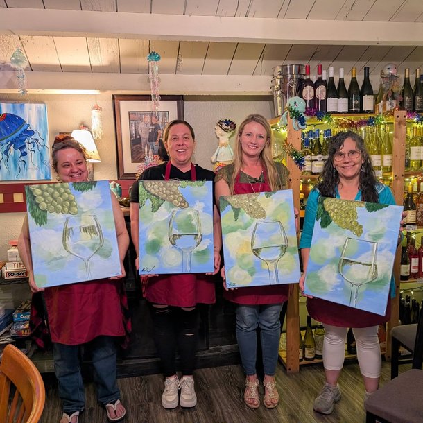 Paint and sip guests holding their paintings at a wine bar